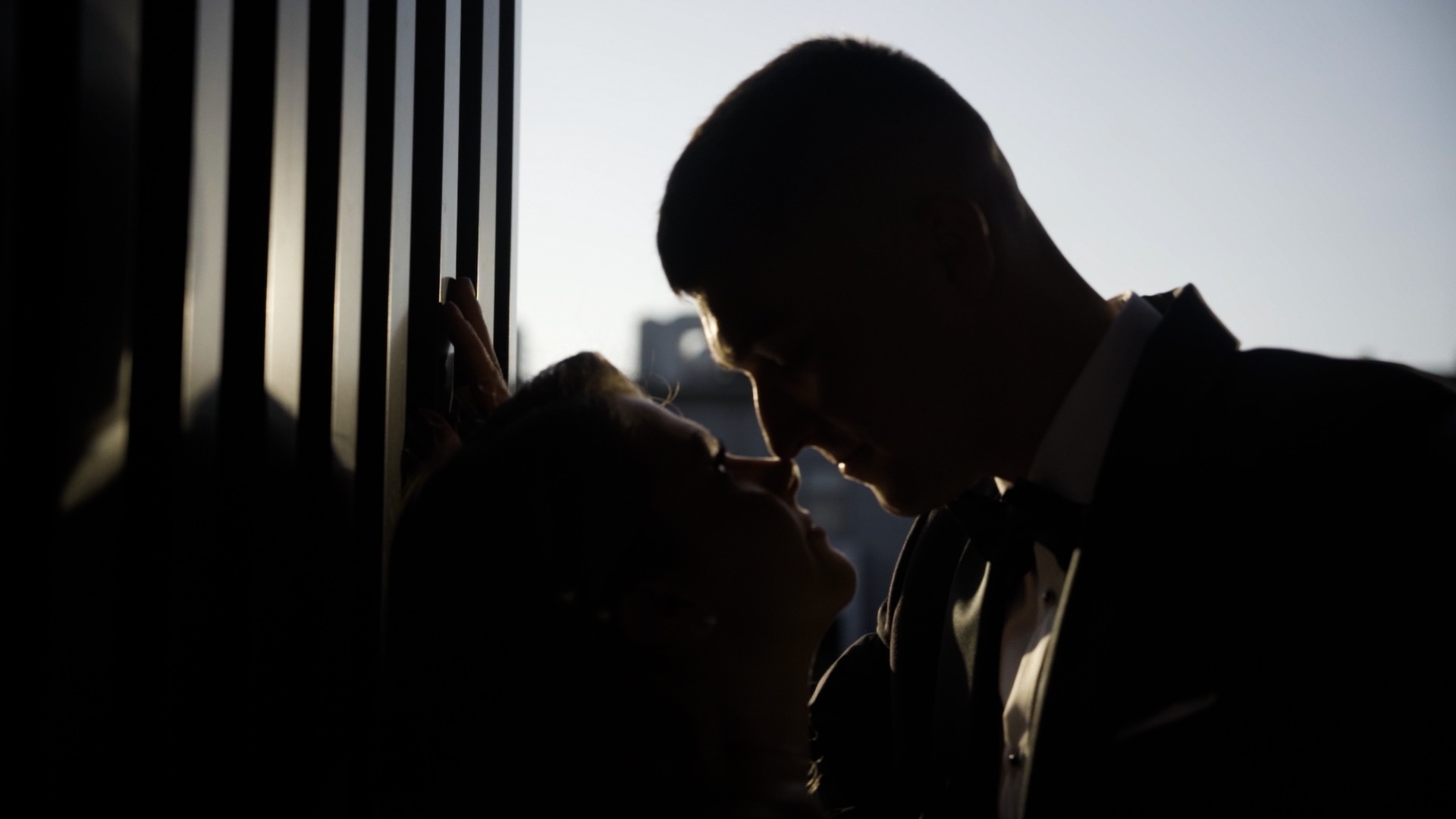 Silhouettes of a bride and groom in a close embrace, captured against a textured wall with natural light highlighting their faces.
