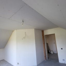 Daniel Janbrw - Poddasze w trakcie adaptacji: zamontowane płyty gipsowo-kartonowe na skośnym suficie, widoczne łączenia i śruby, surowa ściana z wystającymi przewodami, przygotowane do dalszych prac wykończeniowych.