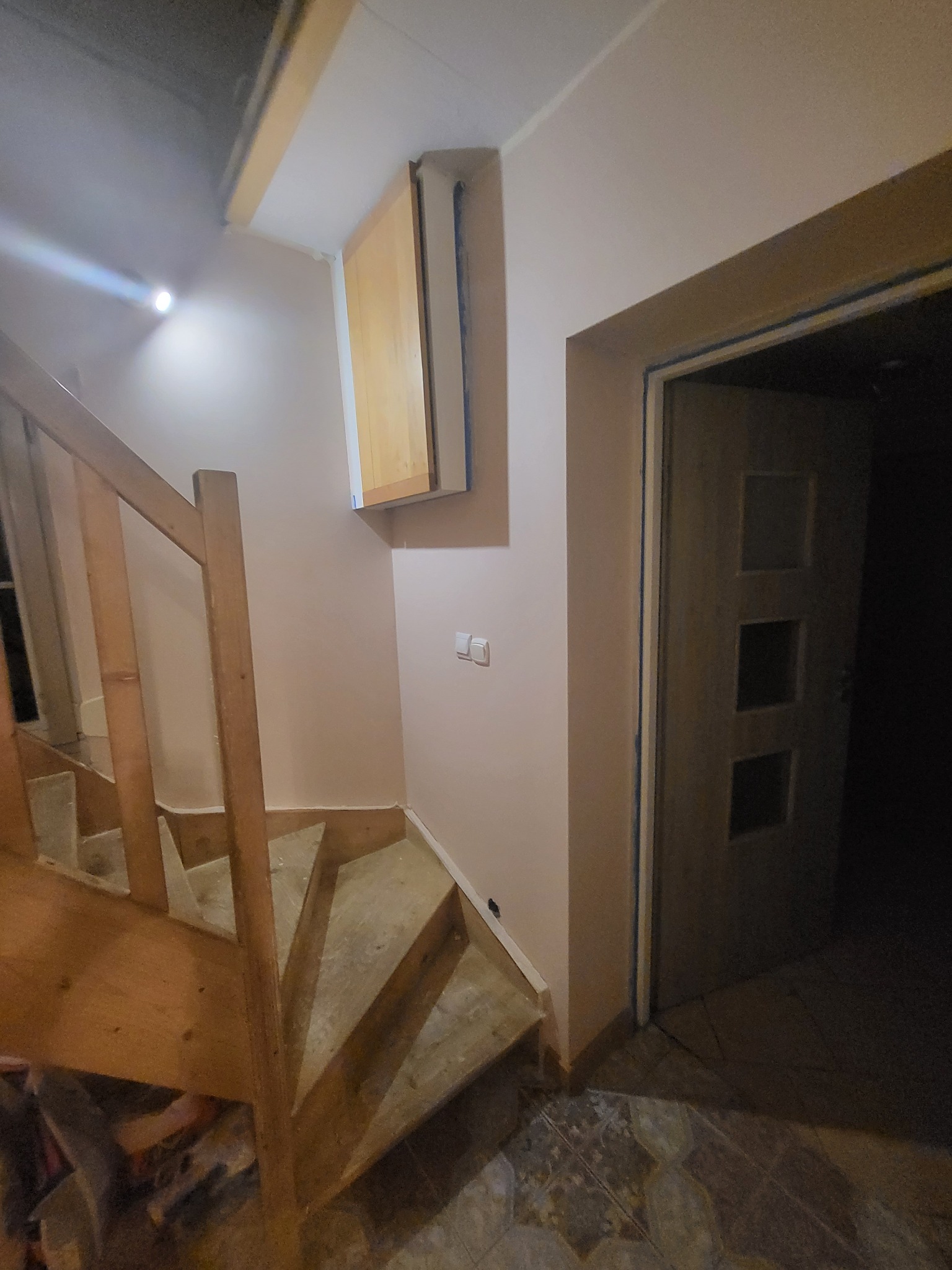 Klatka schodowa w trakcie prac wykończeniowych, ściany świeżo pomalowane na jasny kolor, zabezpieczone taśmą malarską przy futrynie drzwi i listwach przypodłogowych, widoczny fragment drewnianej...