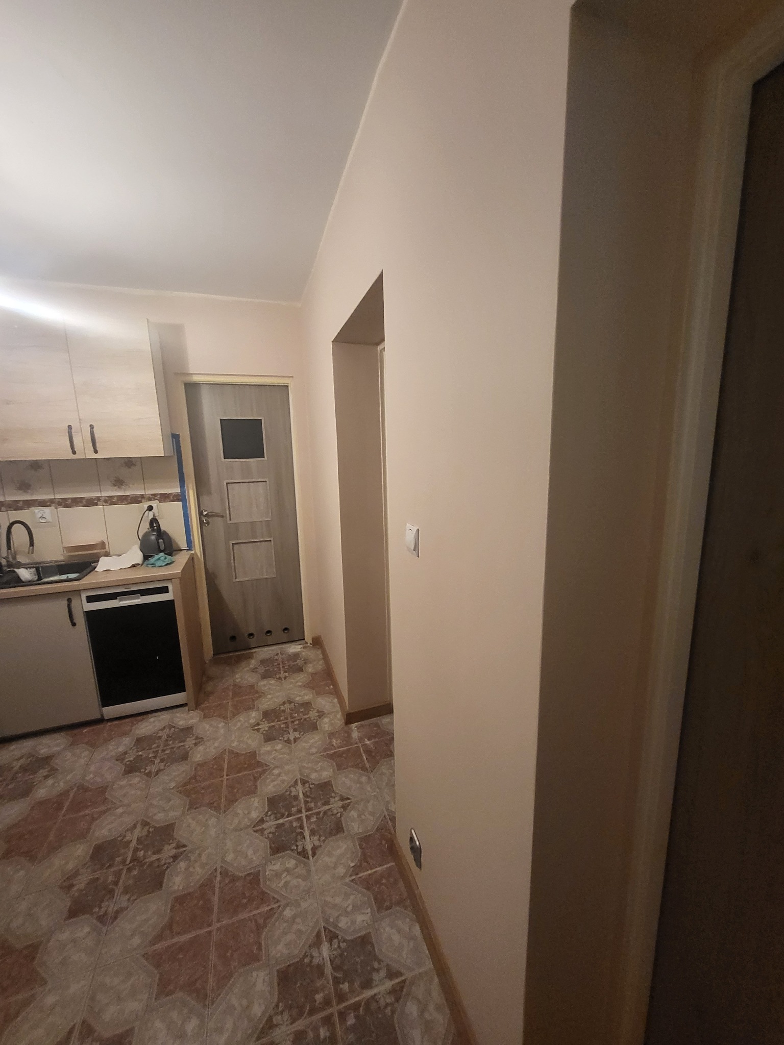 Wnętrze po odświeżeniu w Brwinowie: nowa podłoga z płytek w geometryczny wzór, świeżo pomalowane ściany w odcieniach beżu, widoczny fragment zabudowy kuchennej i drzwi wewnętrzne.