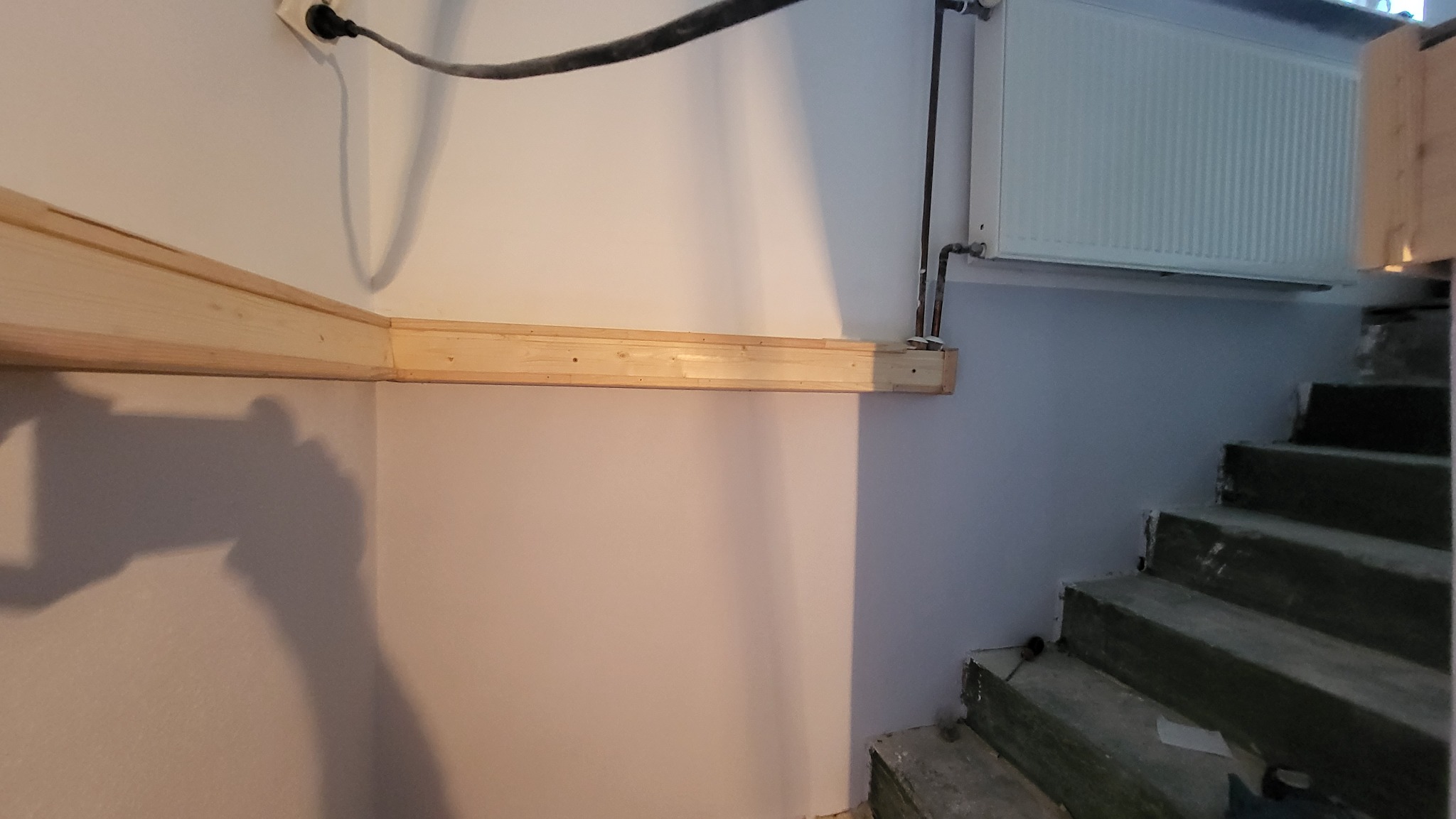 Drewniana konstrukcja pod sufitem, prawdopodobnie pod zabudowę, widoczne przewody elektryczne i fragment schodów w surowym stanie.