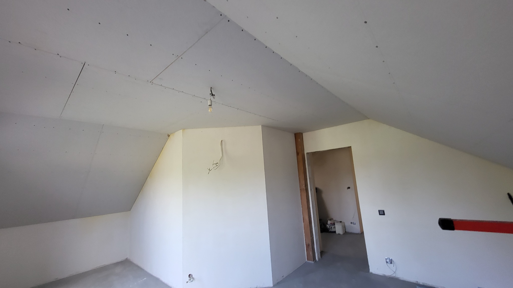 Poddasze w trakcie adaptacji: zamontowane płyty gipsowo-kartonowe na skośnym suficie, widoczne łączenia i śruby, surowa ściana z wystającymi przewodami, przygotowane do dalszych prac wykończeniowych.