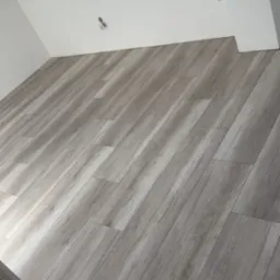 Ukończona podłoga z paneli laminowanych w odcieniach szarości, ułożona w skos w jasnym pokoju na poddaszu z oknem dachowym.