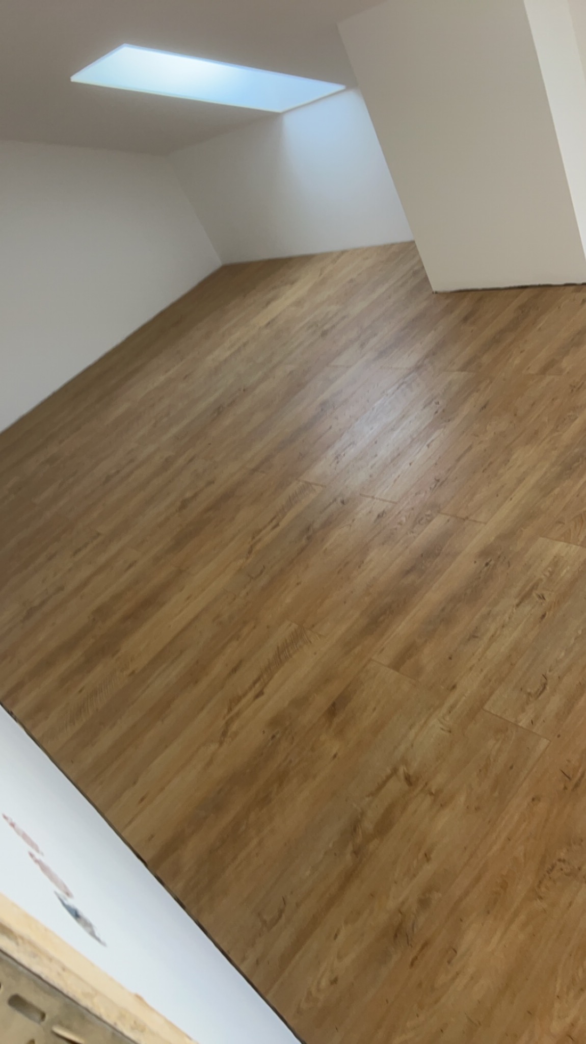 Ukośne ujęcie nowo położonej, jasnobrązowej podłogi laminowanej w jasnym pomieszczeniu na poddaszu ze świetlikiem w suficie.
