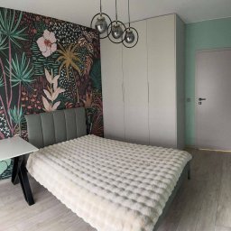 Meble Daniel Cebulski - Pokój z szafą wnękową: wzorzysta tapeta, łóżko z pluszową narzutą i lampy kuliste. Minimalistyczna aranżacja wnętrza sypialni z zabudową meblową.