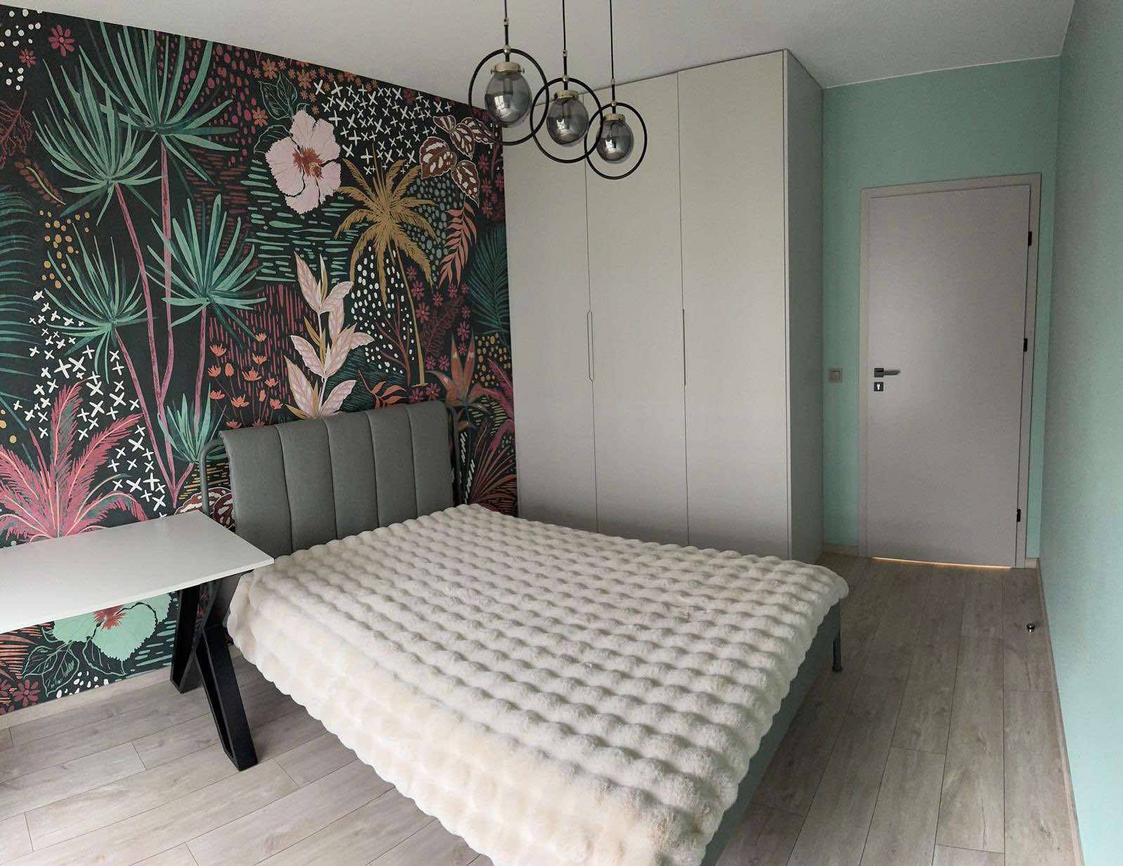 Pokój z szafą wnękową: wzorzysta tapeta, łóżko z pluszową narzutą i lampy kuliste. Minimalistyczna aranżacja wnętrza sypialni z zabudową meblową.