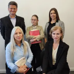 Zespół pięciu osób w biurowym otoczeniu, kobiety trzymają książki, uśmiechają się do kamery.