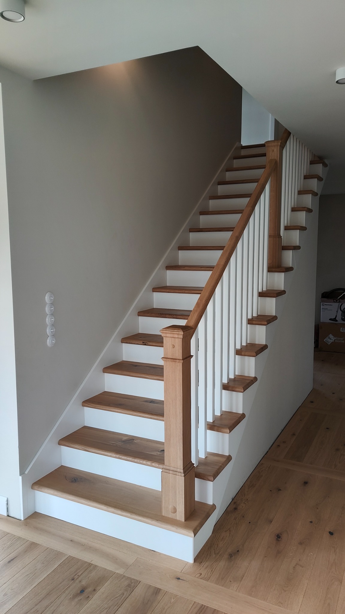 Jasne schody z drewnianymi stopniami i białą balustradą w nowoczesnym wnętrzu, widok od dołu z widocznym fragmentem drewnianej podłogi.