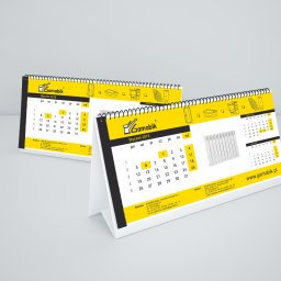 PERFEKTDRUK Joanna Zięba - Dwa kalendarze biurkowe z logo Gamabik na żółtym tle, prezentujące miesiące Styczeń 2015 i Grudzień 2014, z ilustracjami produktów firmy.