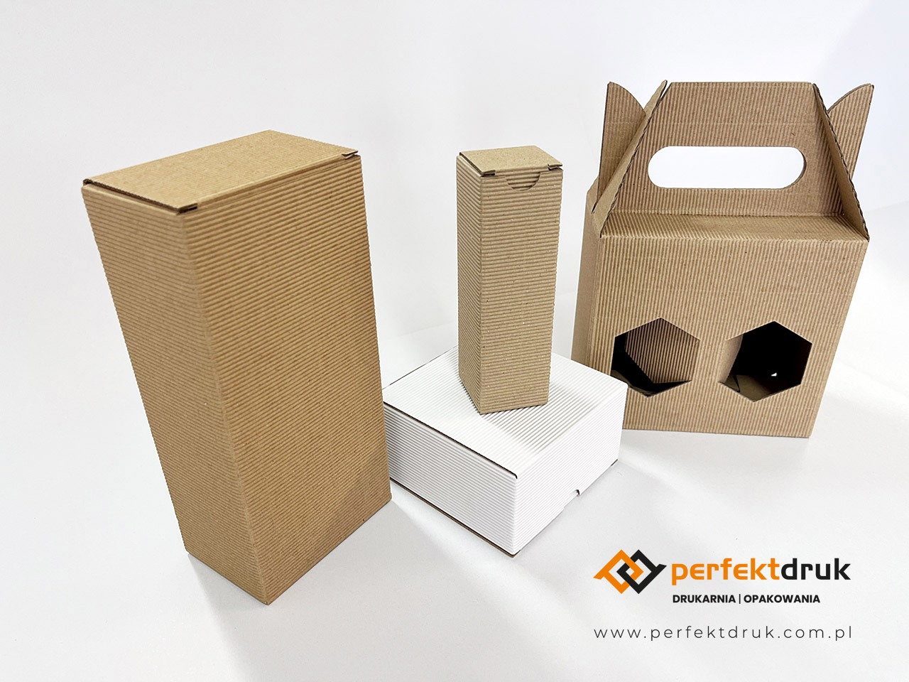 Zdjęcie przedstawia zestaw pudełek z tektury falistej w różnych kształtach i rozmiarach na białym tle, w tym pudełko z uchwytem i otworami w kształcie sześciokątów, z widocznym logo drukarni...
