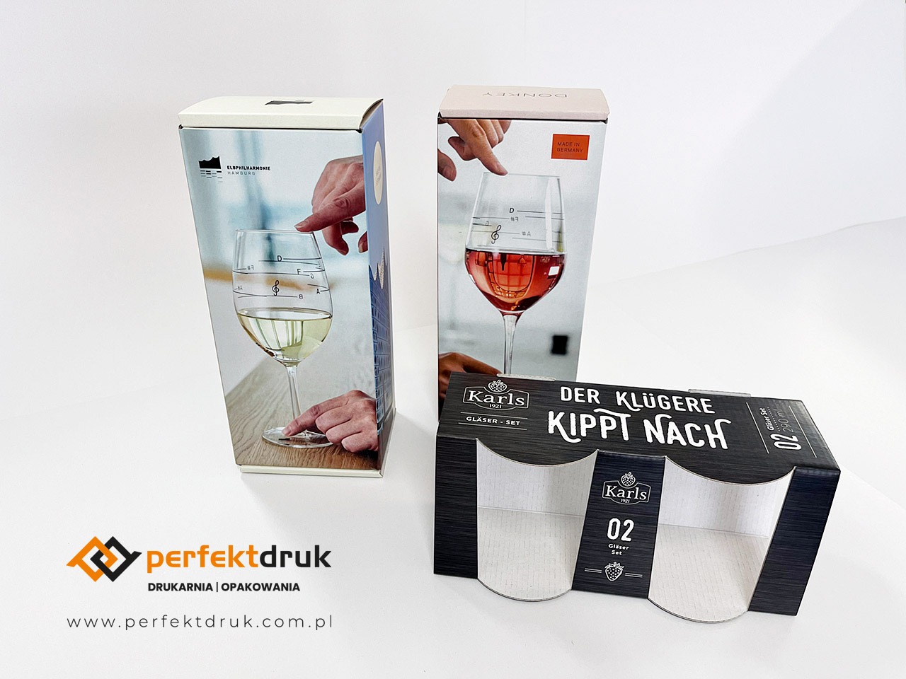 Zestaw pudełek z nadrukiem przedstawiającym kieliszki do wina z nutami, na białym tle, widoczne logo drukarni.