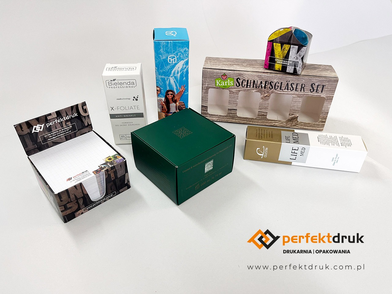 Zestaw różnorodnych opakowań produktowych, w tym pudełka kosmetyczne, opakowanie na szklanki i notatnik z nadrukowanym logo firmy Perfektdruk, prezentowane na białym tle.