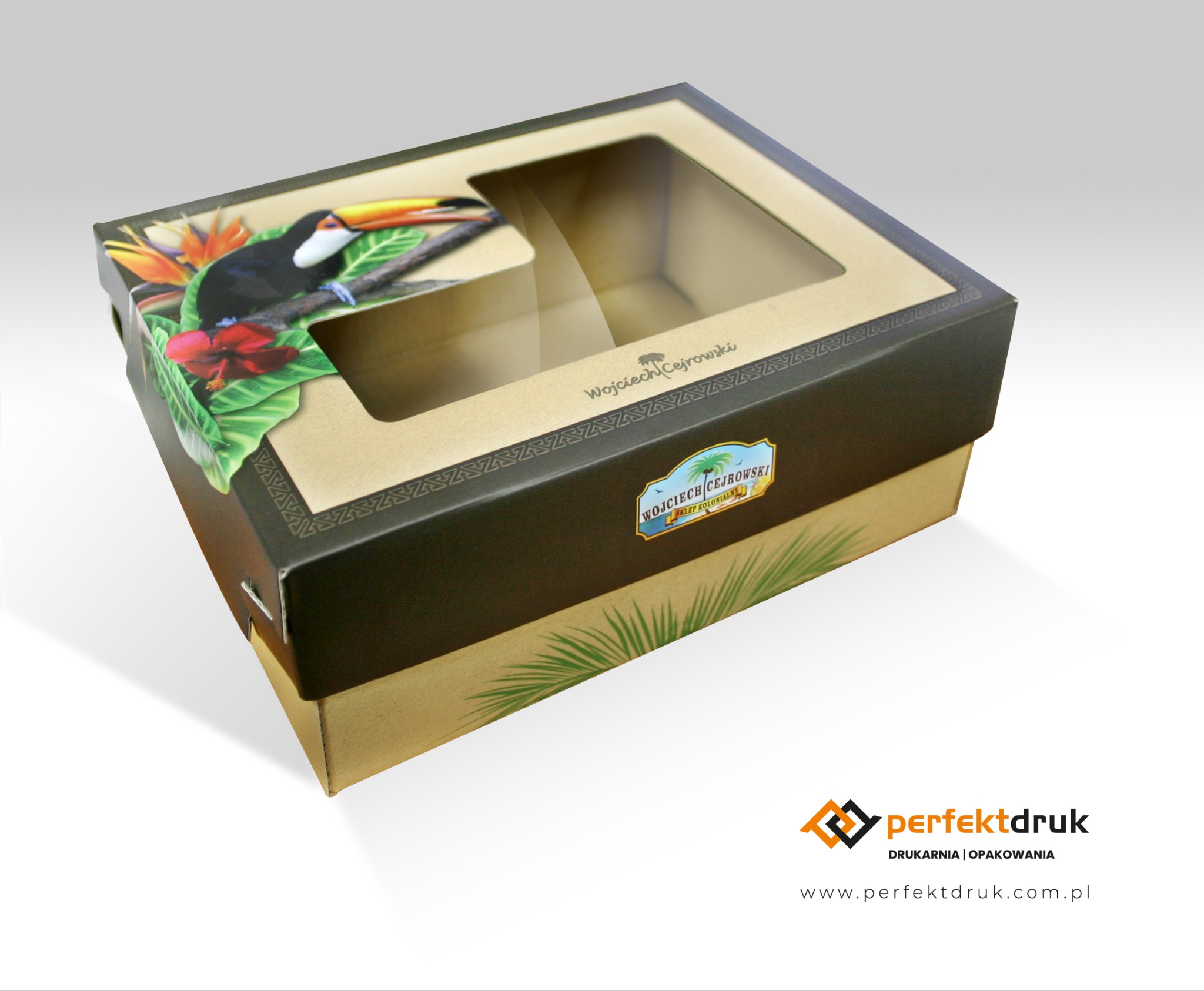 Kartonowe pudełko z okienkiem, zdobione motywem tropikalnym z tukanem i kwiatami, prezentujące branding firmy Wojciech Cejrowski.