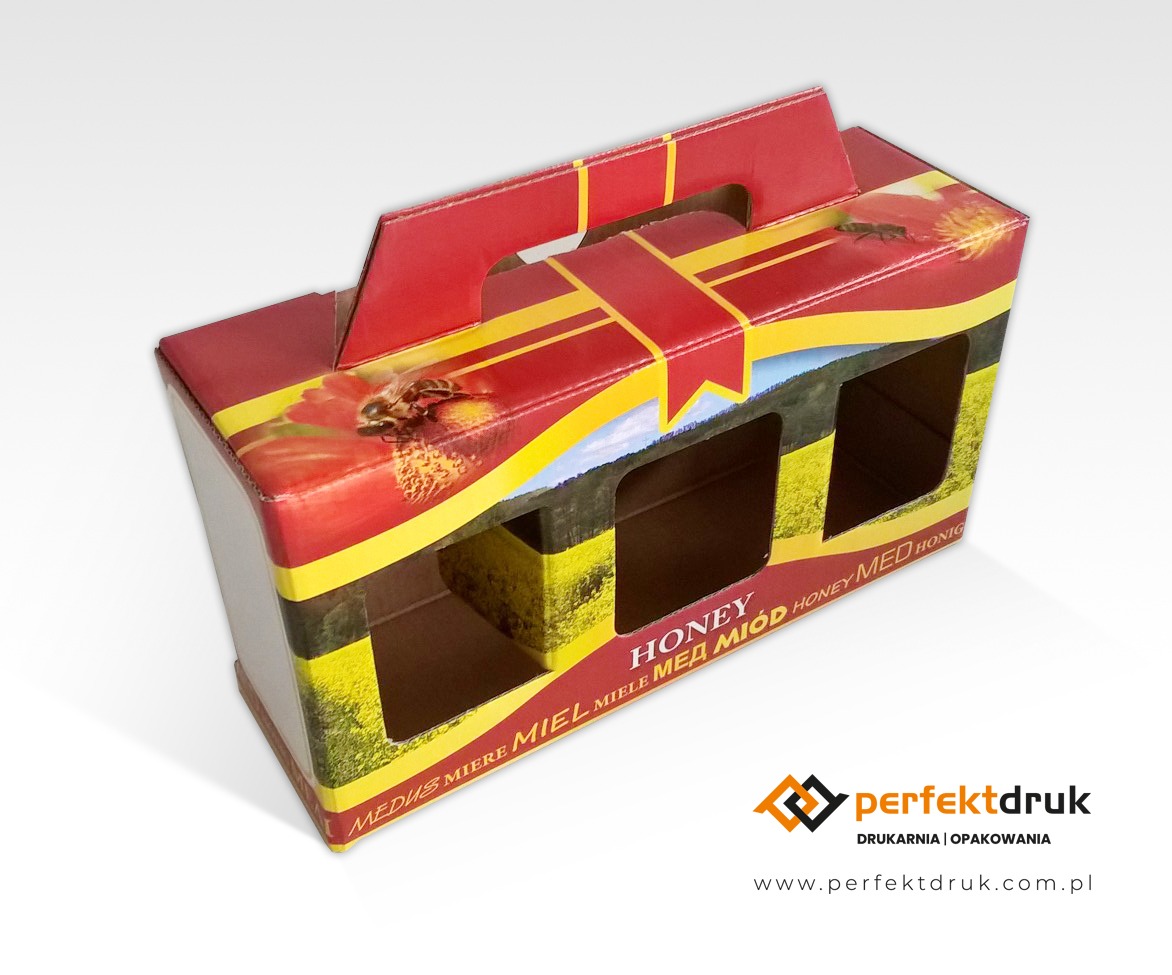 Kartonowe opakowanie z uchwytem na słoiki miodu z nadrukiem motywu kwiatowego i pszczoły, widoczne otwory na słoiki oraz logo drukarni w prawym dolnym rogu.