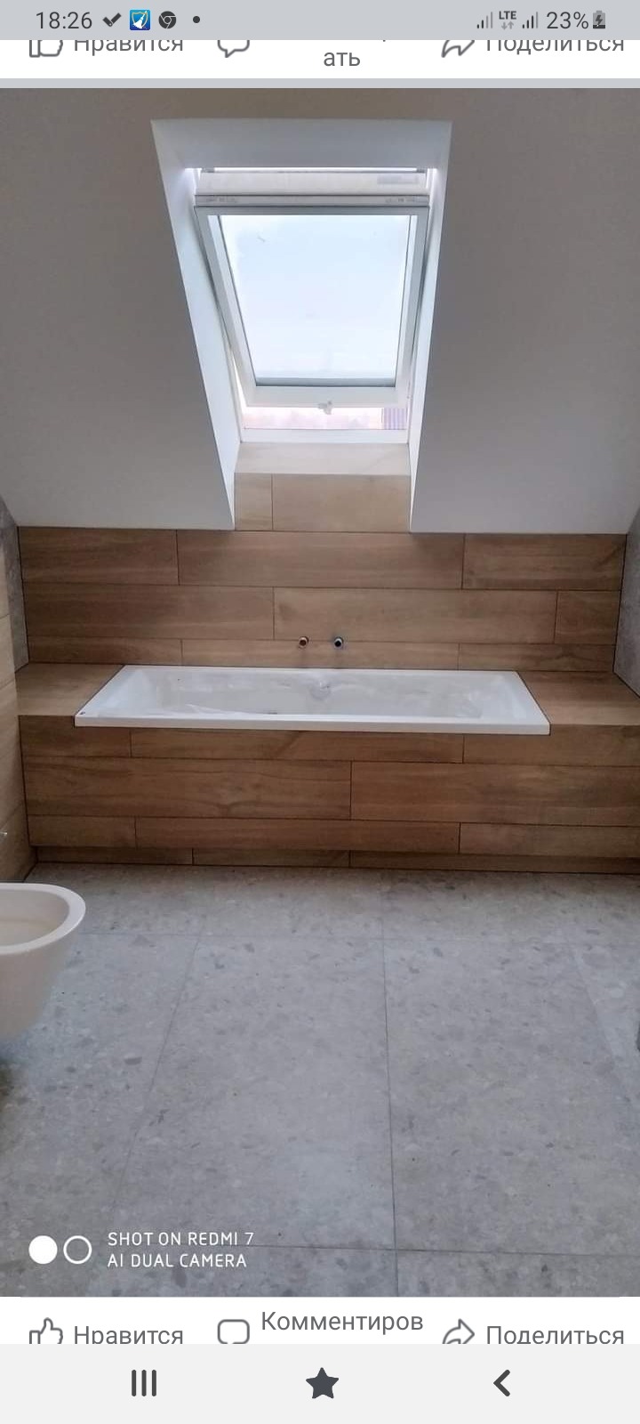 Wykończona łazienka na poddaszu z drewnopodobnymi płytkami, białą wanną i oknem dachowym. Widoczny fragment bidetu.