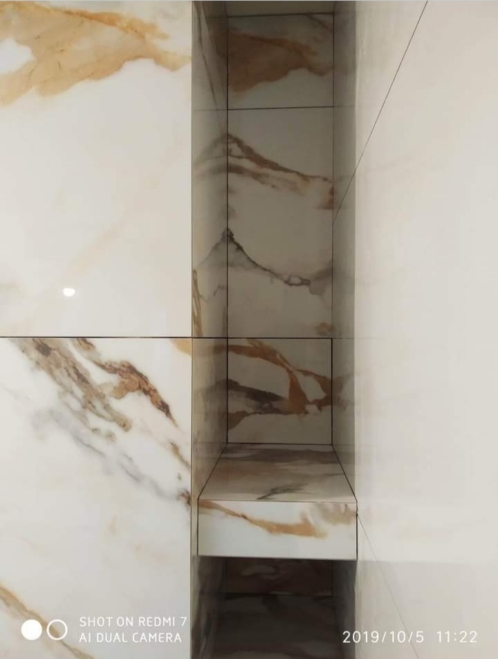 Wnęka w ścianie wyłożona płytkami imitującymi marmur w odcieniach bieli i beżu, z widocznymi fugami i delikatnym załamaniem światła na powierzchni płytek.