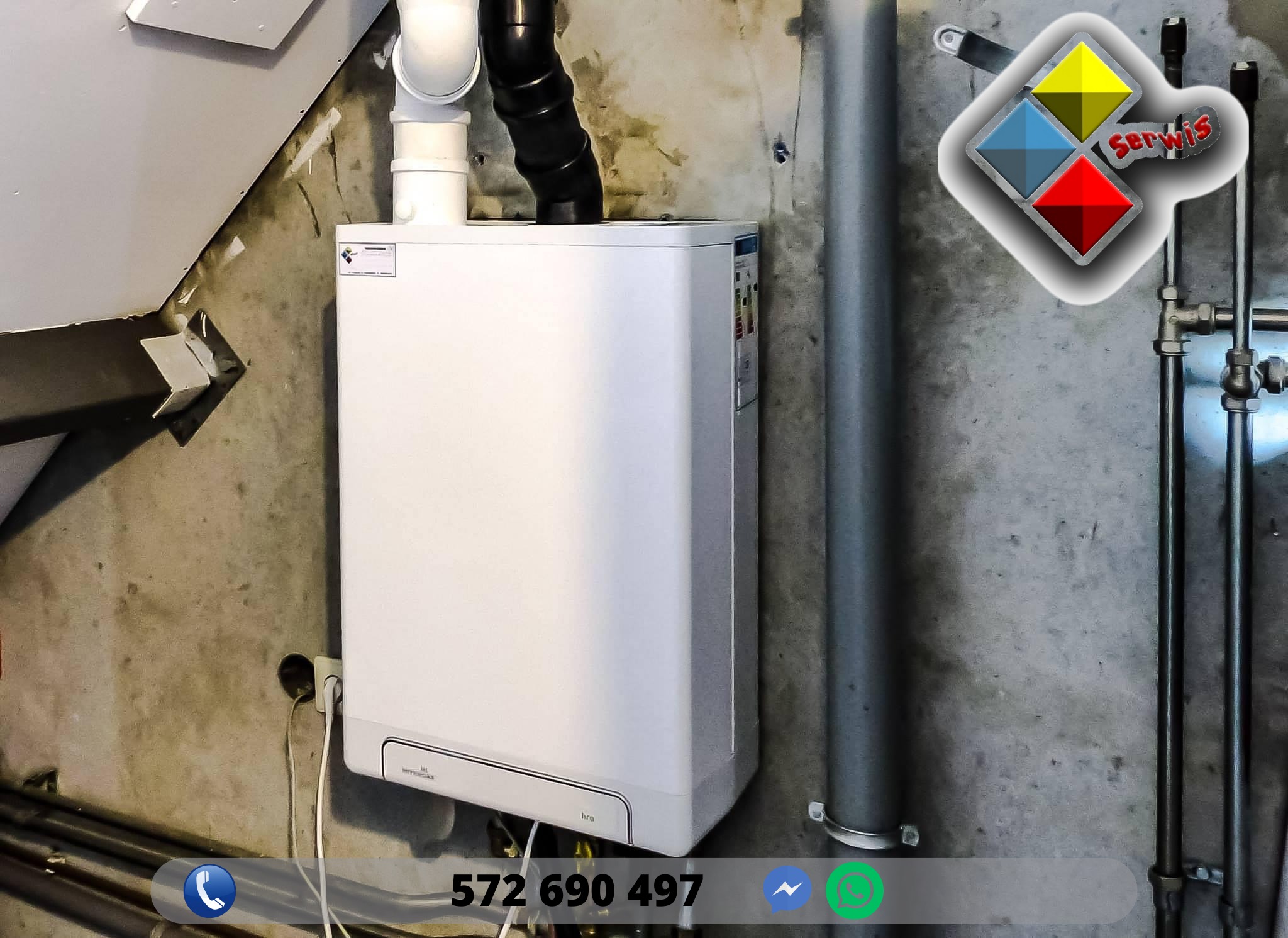 Biały piec grzewczy wiszący na szarej, surowej ścianie, z widocznymi rurami odprowadzającymi spaliny i instalacją hydrauliczną. Naklejka z klasą energetyczną widoczna na boku urządzenia. W rogu...