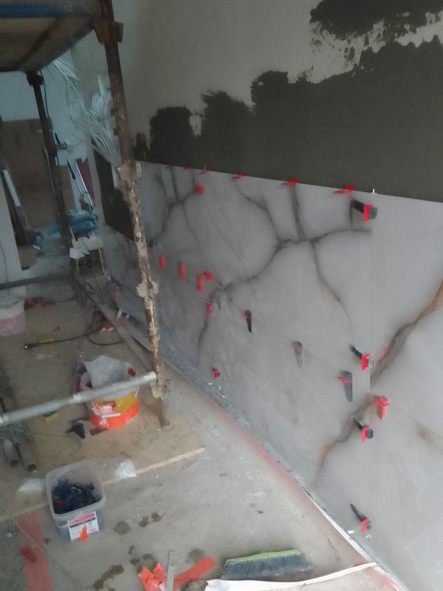 Montaż płytek imitujących marmur na ścianie z użyciem klipsów poziomujących, widoczne rusztowanie i narzędzia glazurnicze.