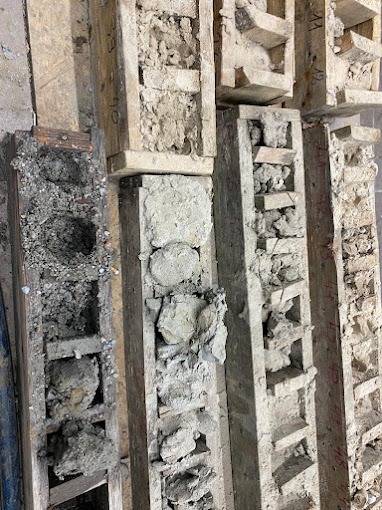 Próbki gruntu w drewnianych formach z widocznymi warstwami, różna konsystencja i skład, dokumentacja geologiczna.