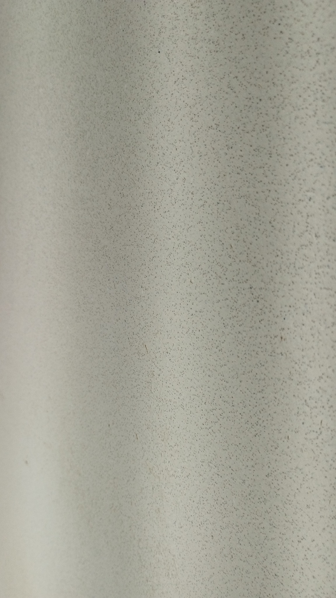 Szara ściana pokryta drobnymi, ciemnymi punktami, tworzącymi delikatną teksturę. Widoczne subtelne cieniowanie.