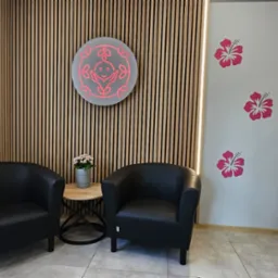 Poczekalnia: Dwa czarne fotele klubowe, okrągły stolik z kwiatami, drewniana ściana z podświetleniem LED, logo i grafika kwiatowa na ścianie, zdjęcie dziecka w ramce.