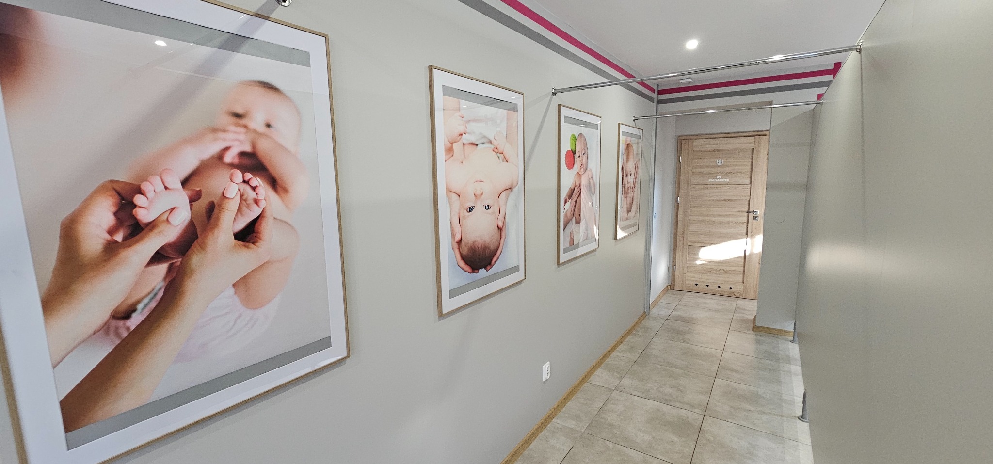 Korytarz gabinetu z powieszonymi oprawionymi zdjęciami niemowląt, w tym zbliżenie na dłonie masujące stopy dziecka.