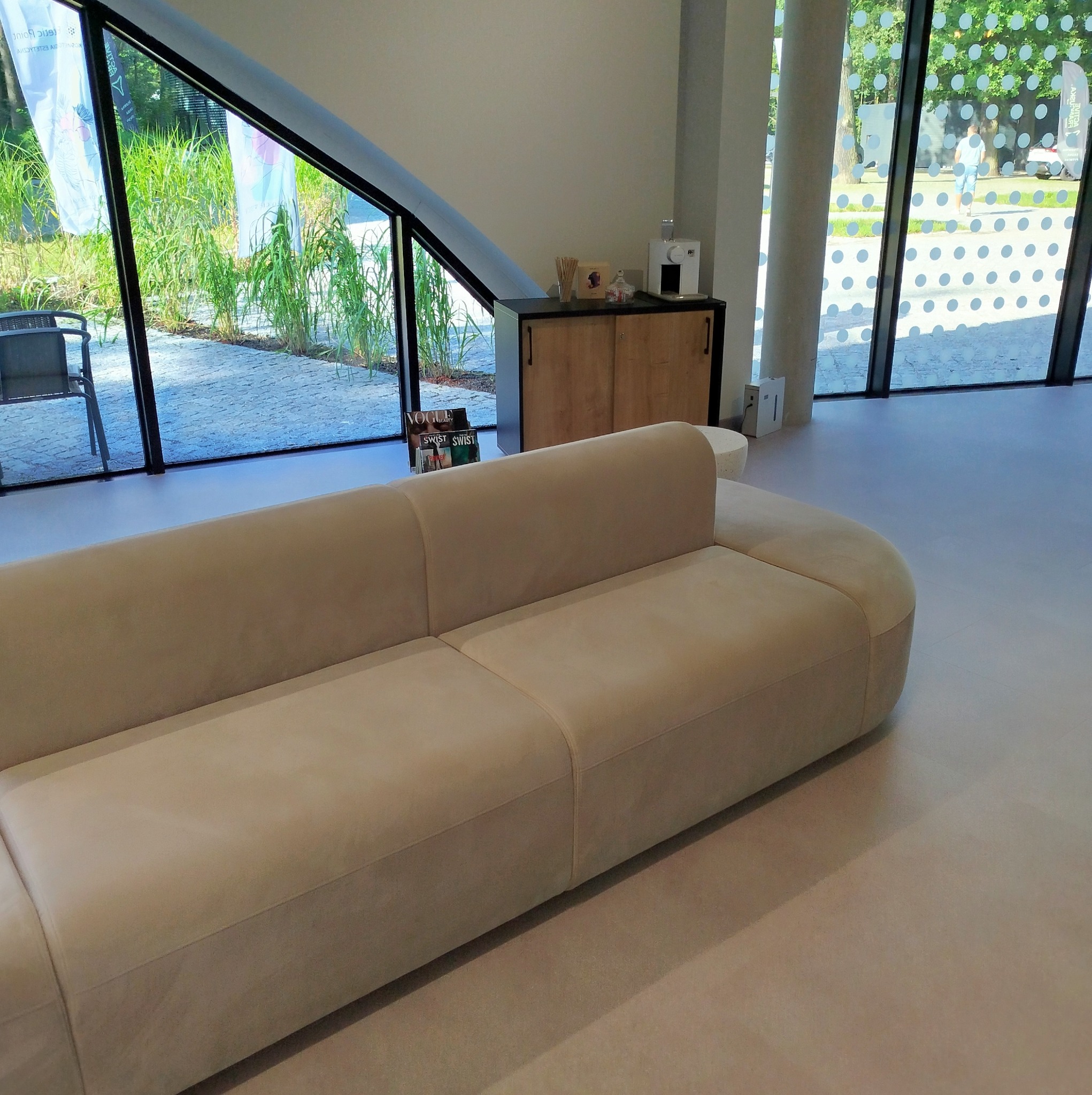 Beżowa sofa modułowa w nowoczesnym biurze z widokiem na zieleń za oknem.