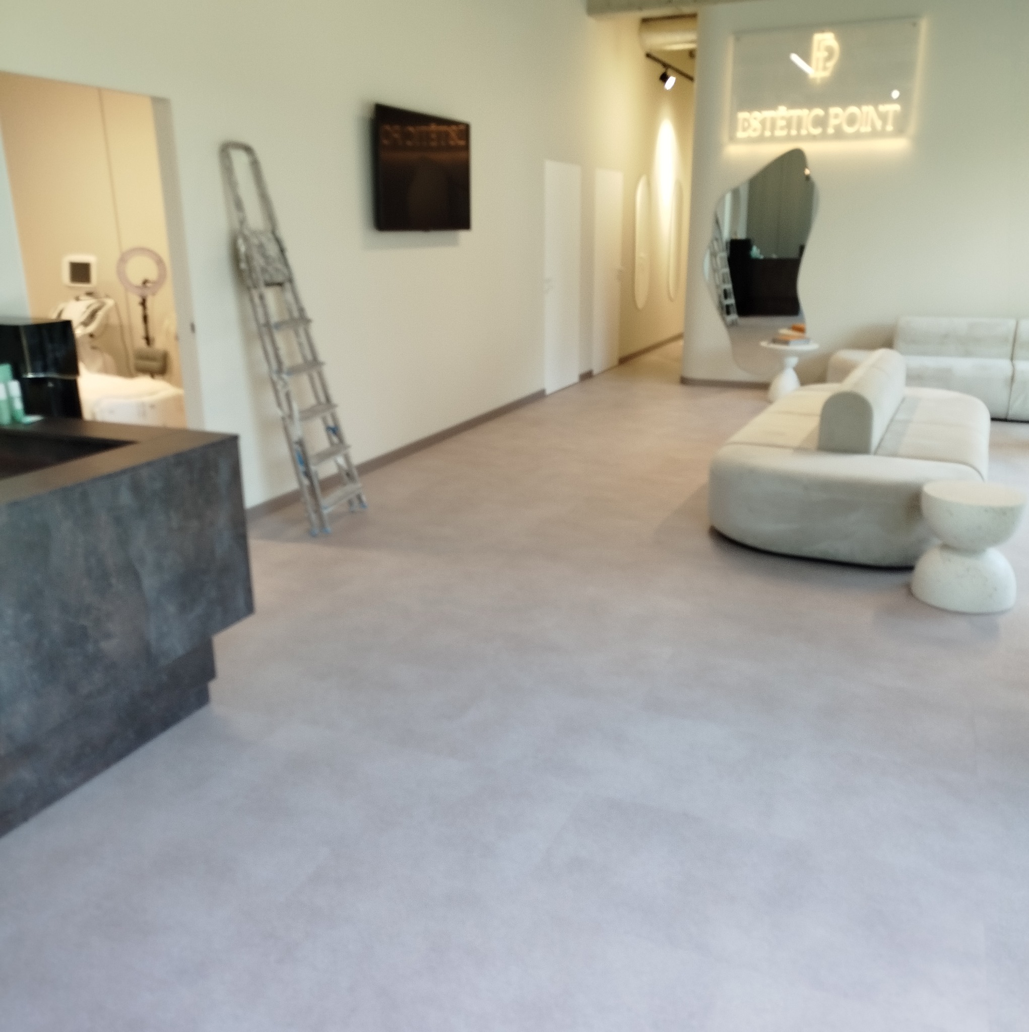 Jasne, minimalistyczne wnętrze biura z elementami dekoracyjnymi: drabina oparta o ścianę, designerskie sofy i stoliki, oraz podświetlany szyld 'Estetic Point'.