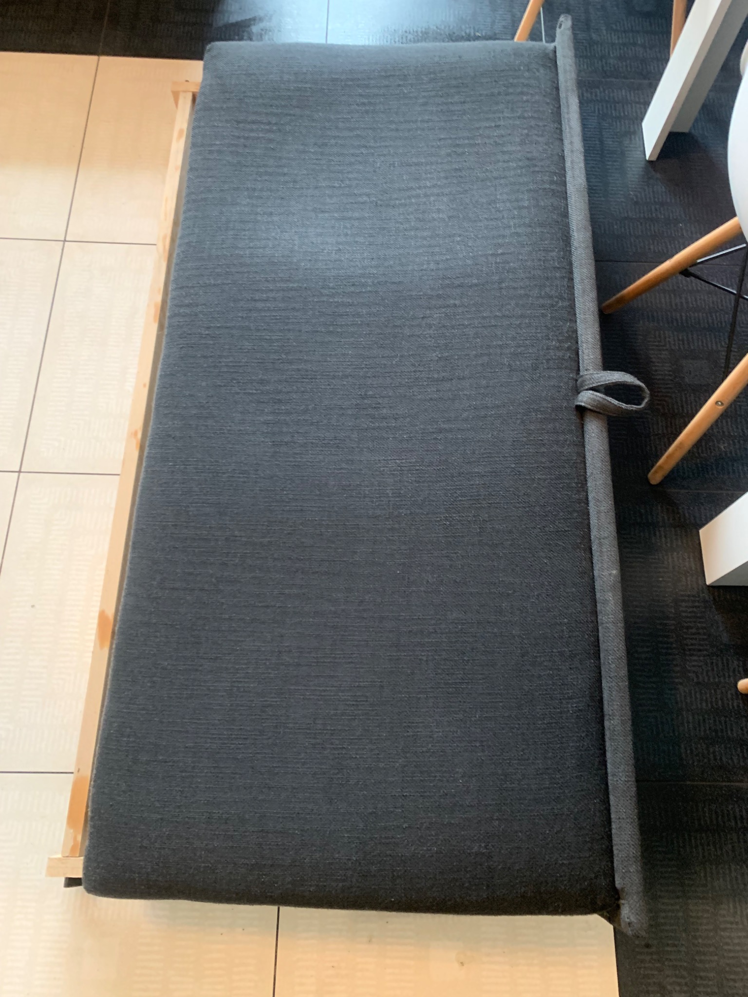 Ciemnoszara tapicerka kanapy z drewnianą ramą, widoczna struktura materiału i detale wykończenia, fragment krzesła w tle.