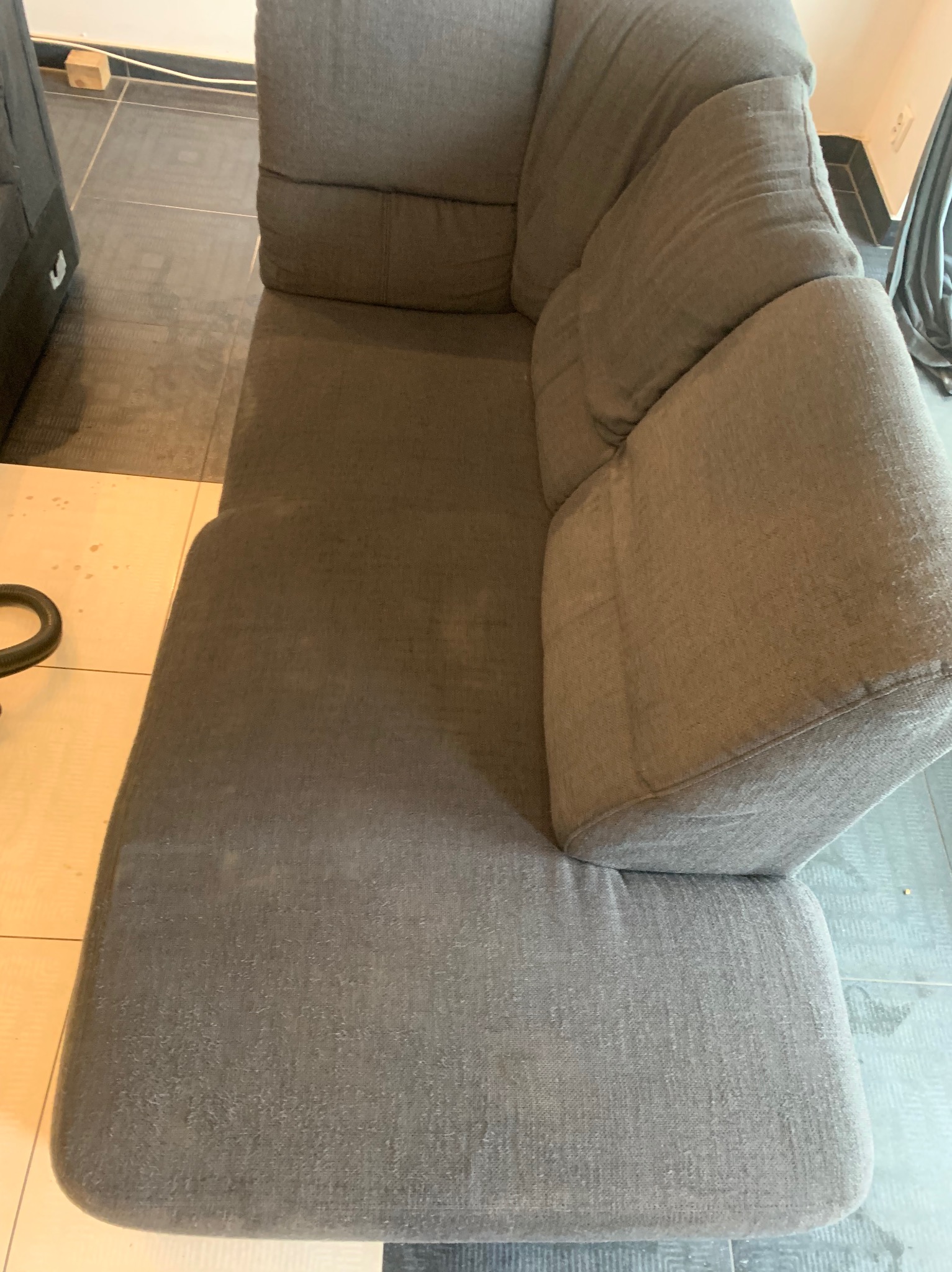 Szara, modułowa kanapa z wyraźnymi śladami użytkowania i plamami na tapicerce, widoczna z góry pod kątem, na tle ceramicznej podłogi.