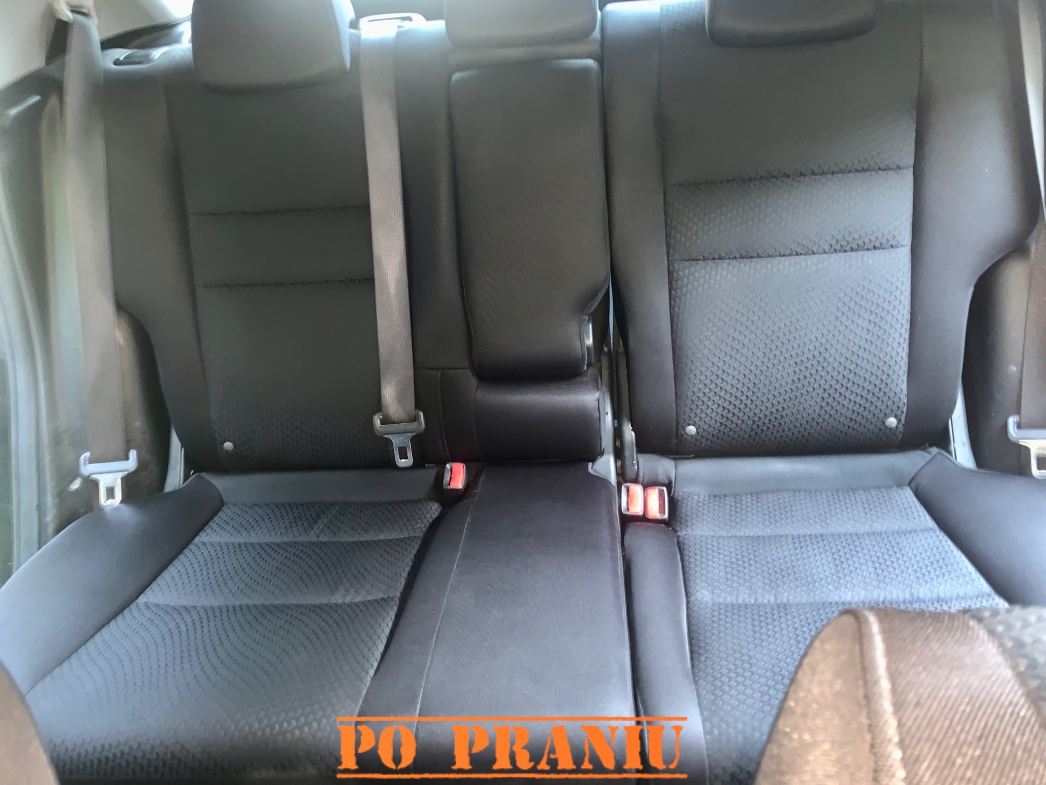 Wnętrze samochodu z widoczną tylną kanapą po czyszczeniu, ukazującą odświeżoną tapicerkę z wyraźnym wzorem i pasami bezpieczeństwa.