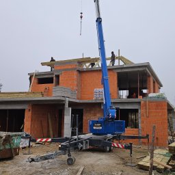 PHU PERFECT BUD MATEUSZ SPYTEK - Budowa domu jednorodzinnego w stanie surowym otwartym, z widocznym dźwigiem teleskopowym, pustakami ceramicznymi i drewnianą konstrukcją dachu w trakcie montażu.