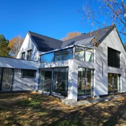 Nowoczesny dom jednorodzinny w Serocku z jasną elewacją i przeszkloną werandą, widok z zewnątrz w jesiennej scenerii.