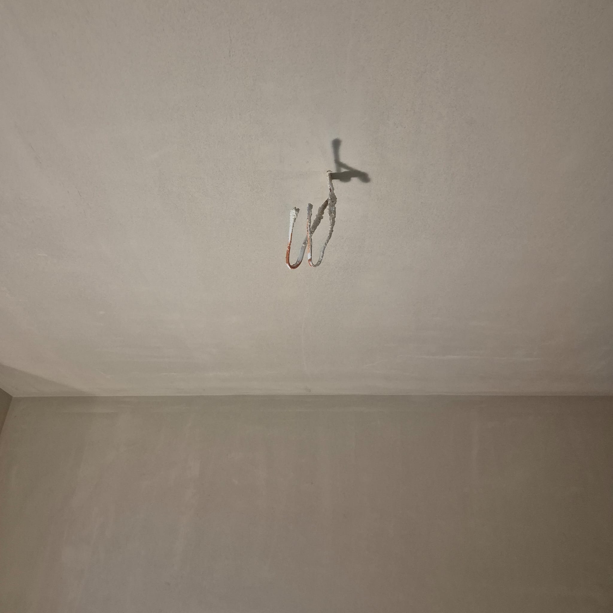 Wnętrze w trakcie prac wykończeniowych: ściany i sufit po nałożeniu gładzi, widoczne wystające przewody elektryczne.