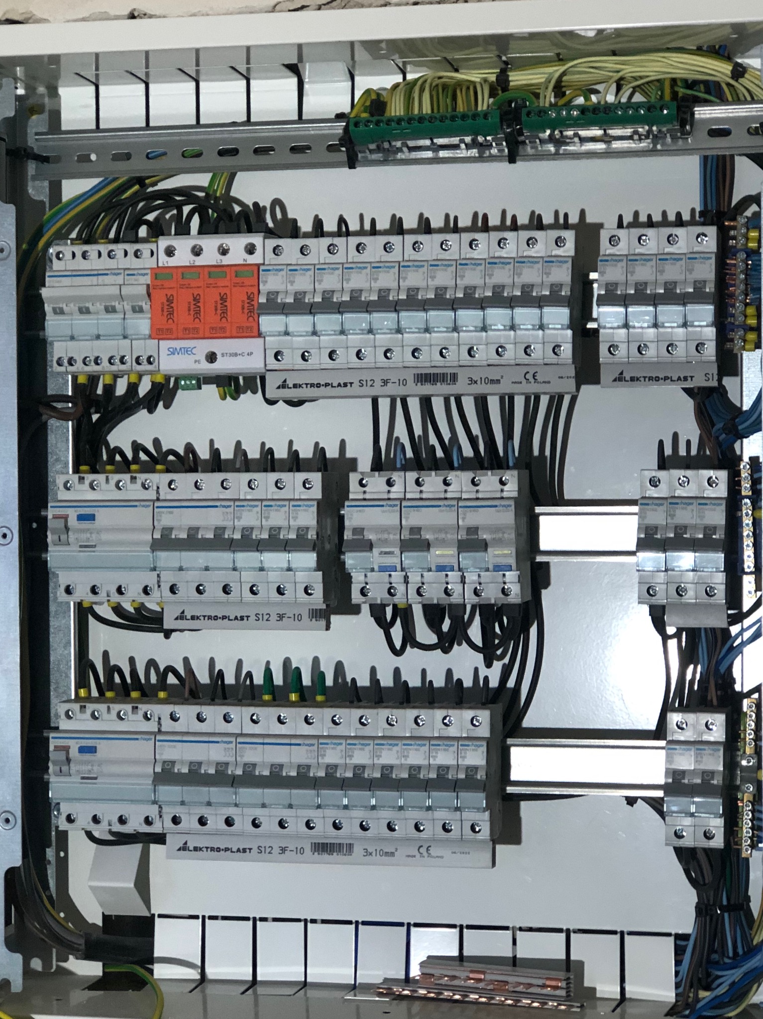 Rozdzielnica elektryczna z zainstalowanymi bezpiecznikami, zabezpieczeniami przepięciowymi i przewodami, widoczne elementy marki Hager i Elektro-Plast.