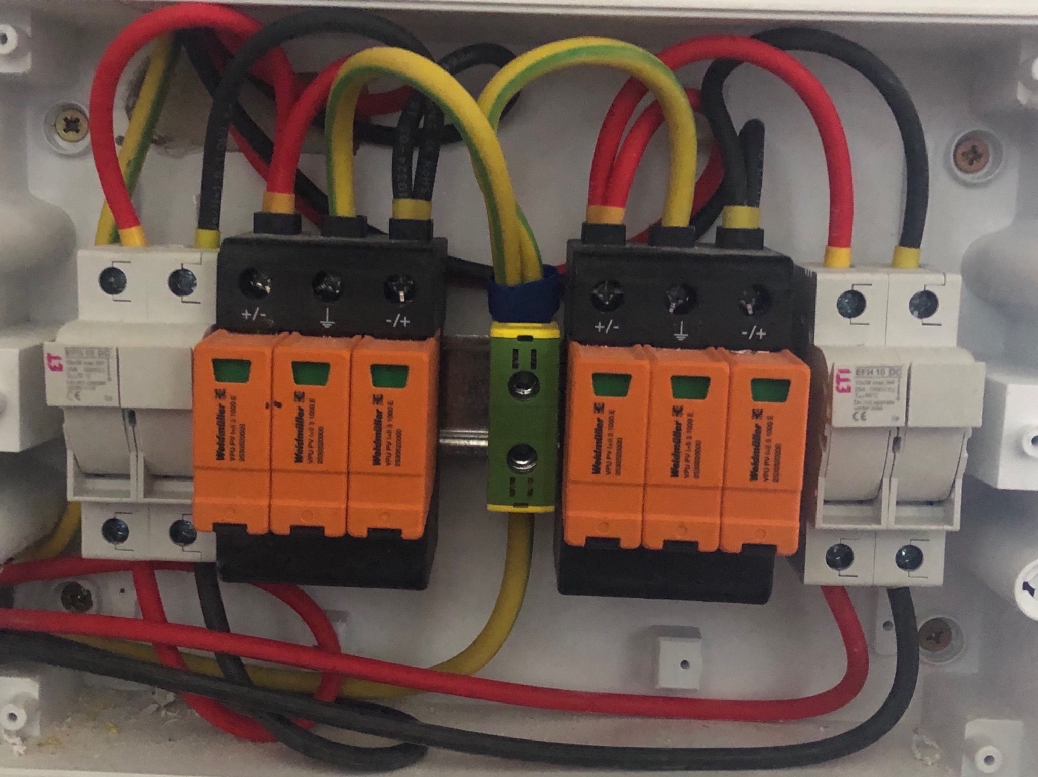 Rozdzielnica elektryczna z zamontowanymi ogranicznikami przepięć Weidmuller VPU PV, z widocznymi przewodami w kolorach czerwonym, czarnym i żółto-zielonym, w białej obudowie.