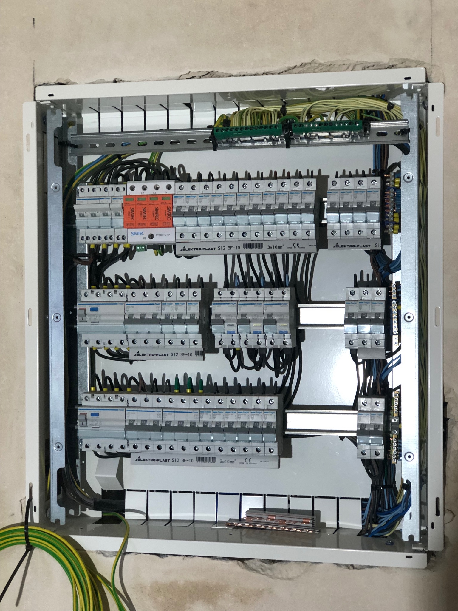 Otwarta skrzynka rozdzielcza z zamontowanymi bezpiecznikami i przewodami, widoczne elementy montażowe i listwy zaciskowe, ściana z surowym wykończeniem w tle.