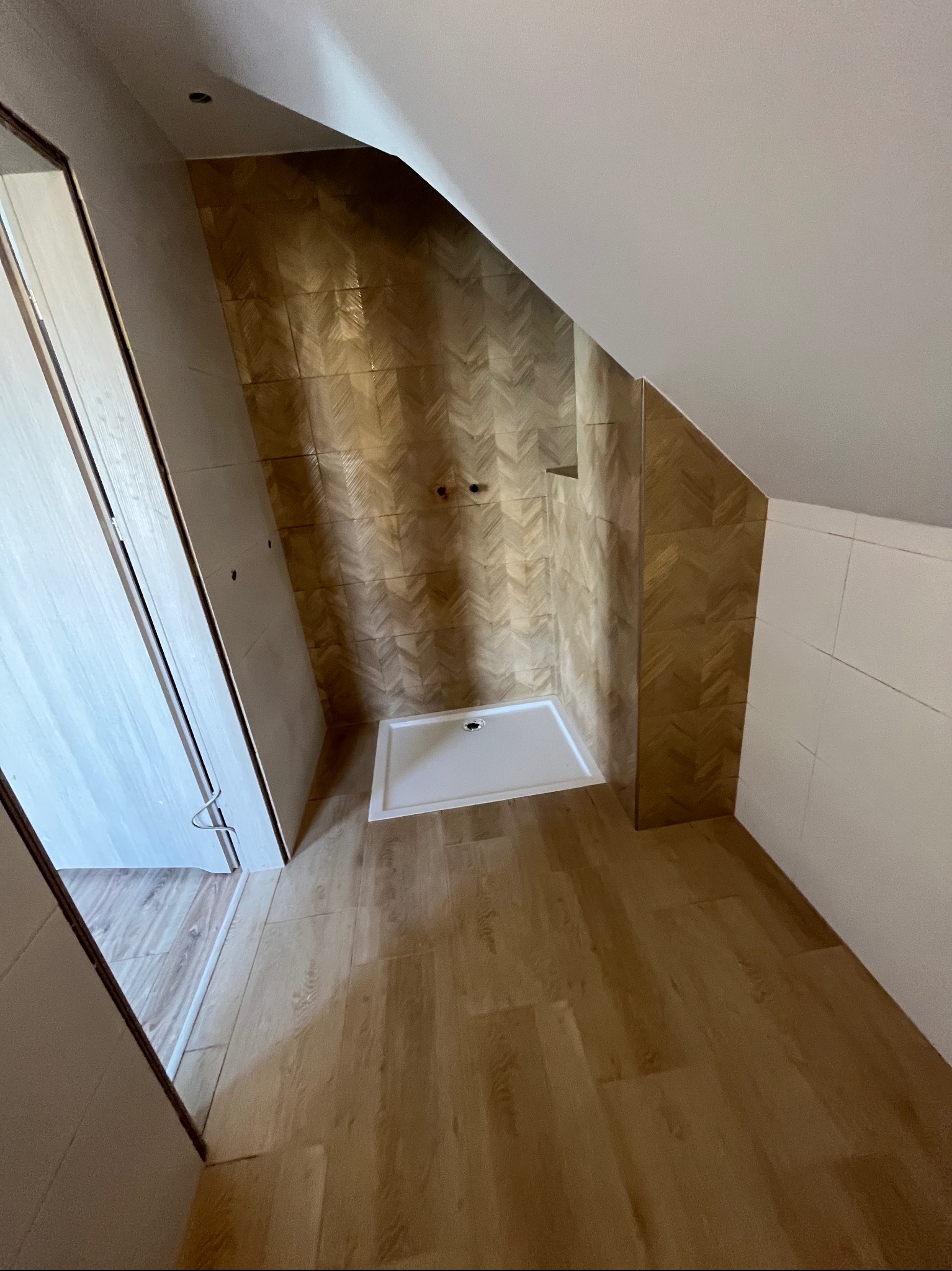 Wykończona łazienka na poddaszu ze złotymi płytkami ułożonymi w jodełkę. Nowa kabina prysznicowa i panele podłogowe imitujące drewno.