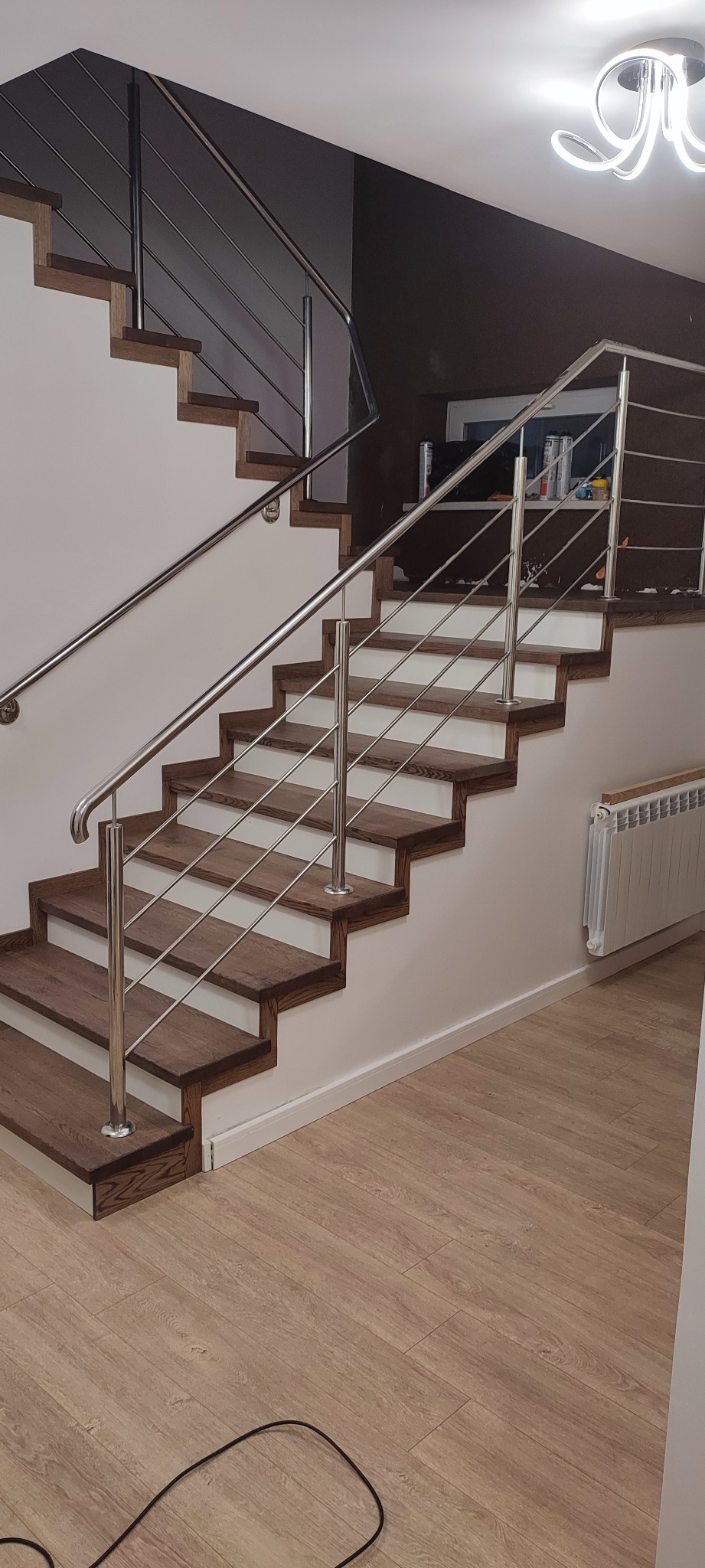 Nowoczesne schody drewniane z metalową balustradą, widok z dołu, oświetlenie sufitowe, jasne ściany.