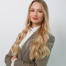 juliah.Fotografia - Portret kobiety z blond włosami w brązowym tweedowym żakiecie i białej koszuli, pozującej na jasnym tle z założonymi rękami.