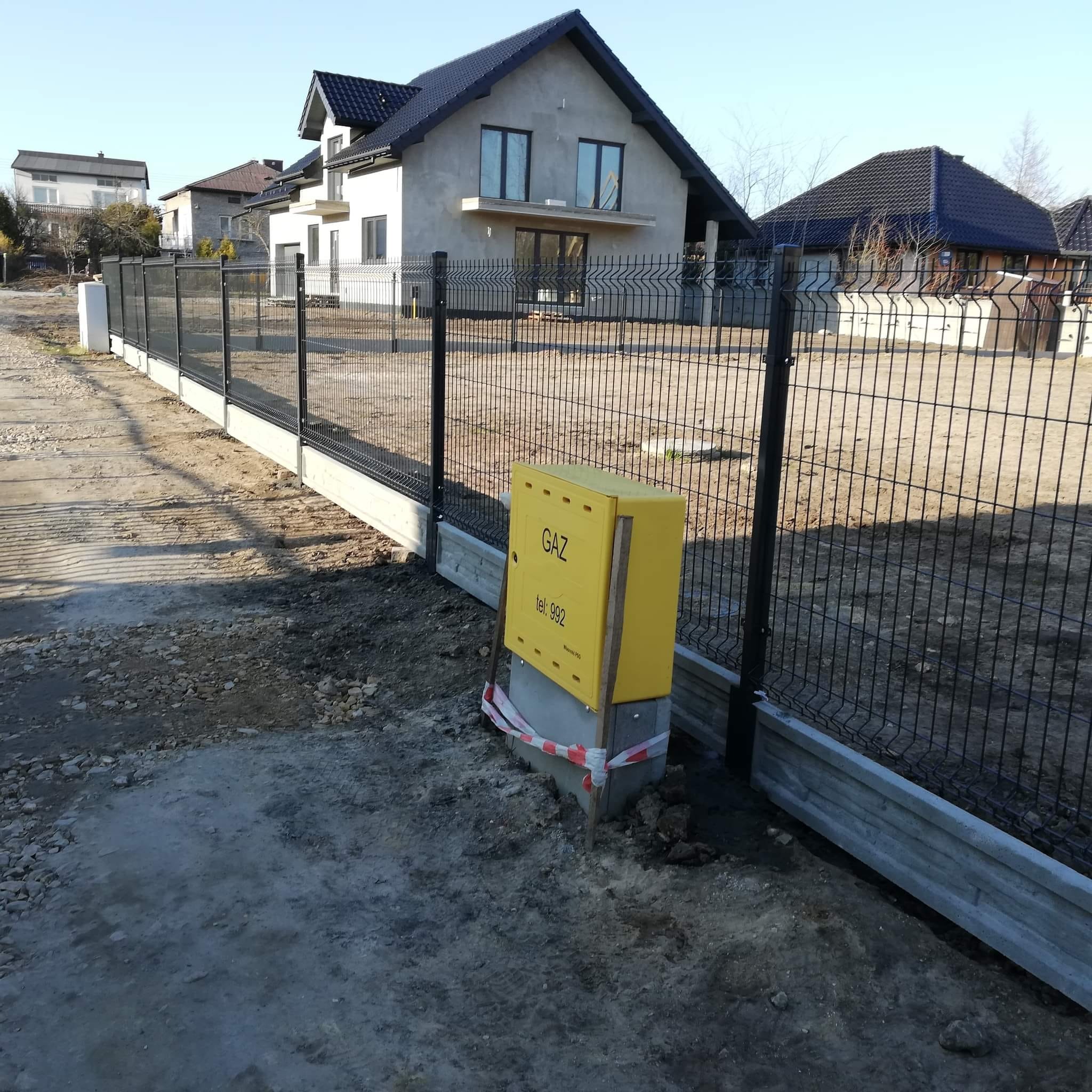 Nowoczesne ogrodzenie panelowe z podmurówką betonową w trakcie montażu, widoczna żółta skrzynka gazowa z napisem 'GAZ' i taśma ostrzegawcza.