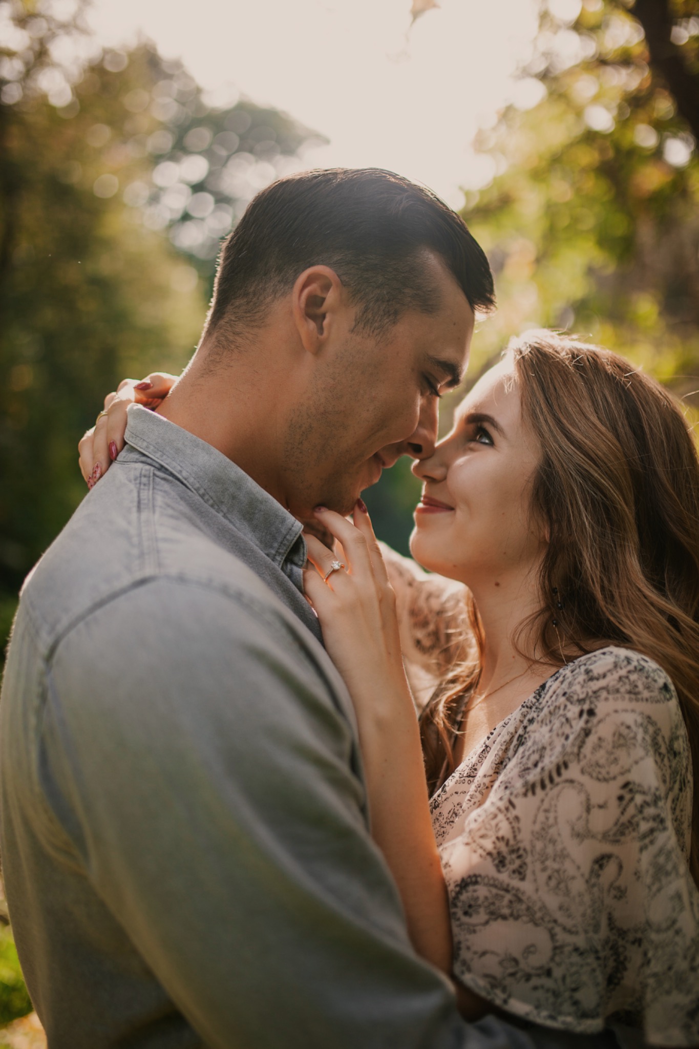 Zakochana para w objęciach, ona z pierścionkiem zaręczynowym, delikatne promienie słońca w tle.