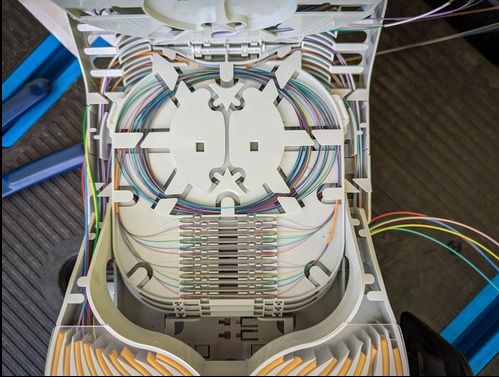 Otwarta skrzynka z uporządkowanymi kablami światłowodowymi wewnątrz, widok z góry, z elementami montażowymi i różnokolorowymi przewodami.
