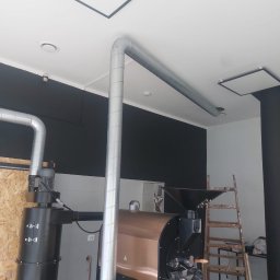 INVEST DL SPÓŁKA Z OGRANICZONĄ ODPOWIEDZIALNOŚCIĄ - System wentylacyjny z metalowymi rurami odprowadzającymi powietrze od pieca do palenia kawy, widoczna drabina oparta o ścianę.