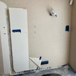 INVEST DL SPÓŁKA Z OGRANICZONĄ ODPOWIEDZIALNOŚCIĄ - Przygotowanie ściany pod montaż jednostki wewnętrznej: odkryte przewody elektryczne, otwory w ścianie zabezpieczone taśmą malarską, częściowo odsłonięta instalacja w ścianie, widoczny fragment...