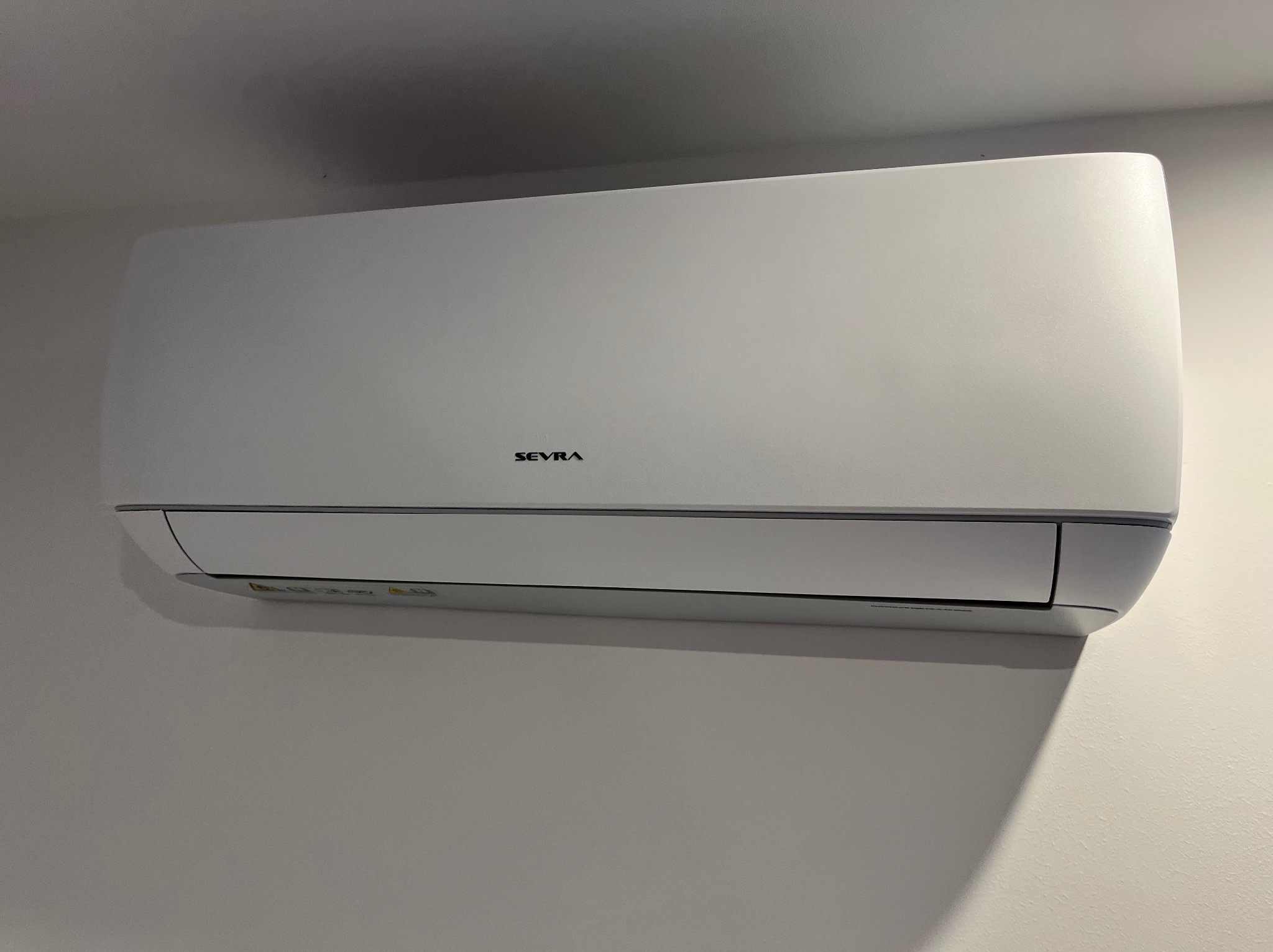 Biały klimatyzator marki SEVRA zamontowany na jasnej ścianie w pomieszczeniu.
