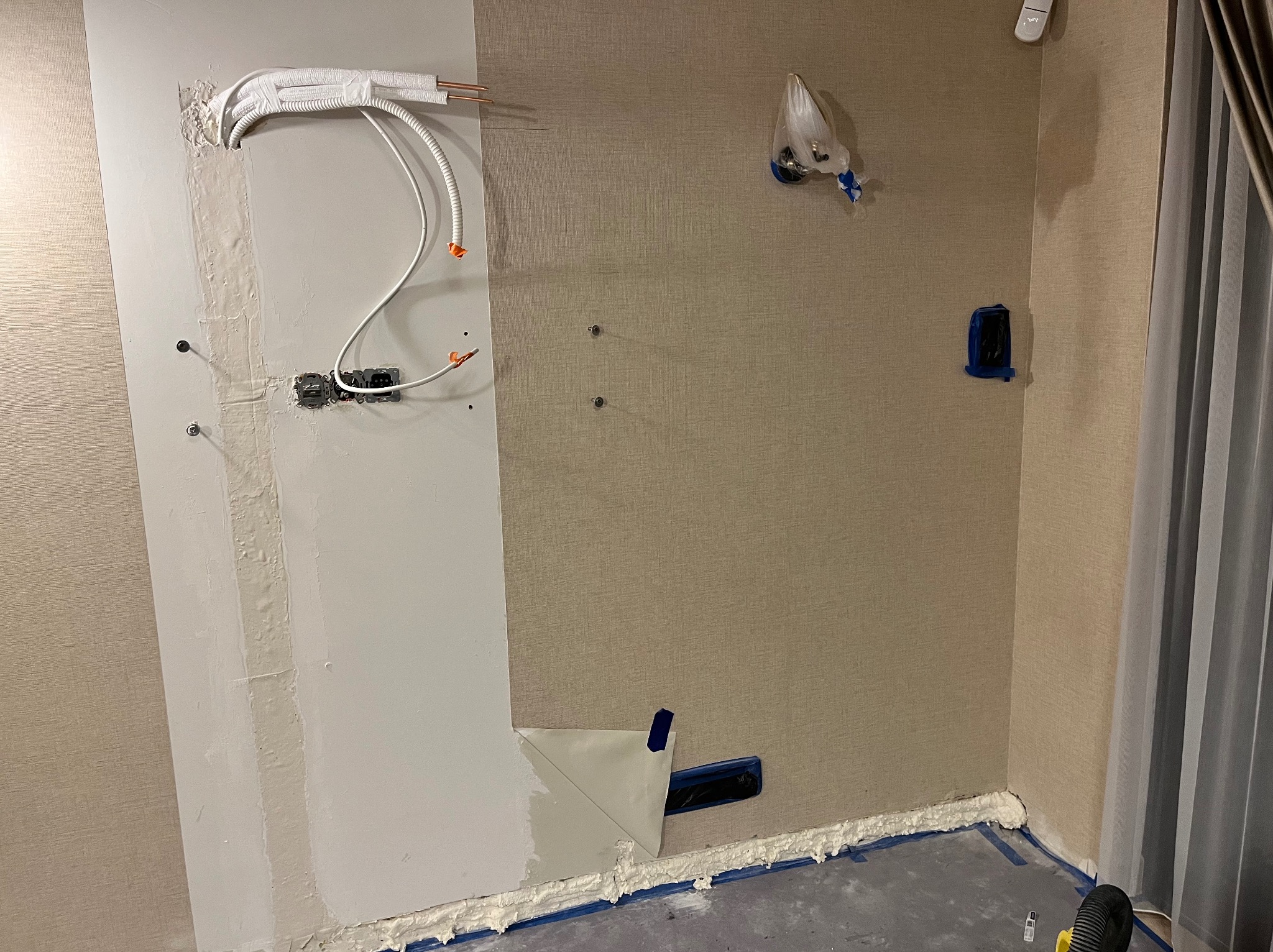 Montaż klimatyzacji w domu: widoczne przewody chłodnicze, instalacja elektryczna w ścianie, zabezpieczone elementy, pianka montażowa przy podłodze.