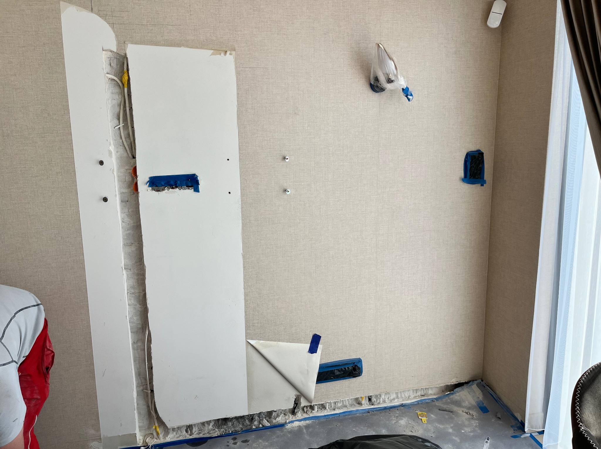 Przygotowanie ściany pod montaż jednostki wewnętrznej: odkryte przewody elektryczne, otwory w ścianie zabezpieczone taśmą malarską, częściowo odsłonięta instalacja w ścianie, widoczny fragment...