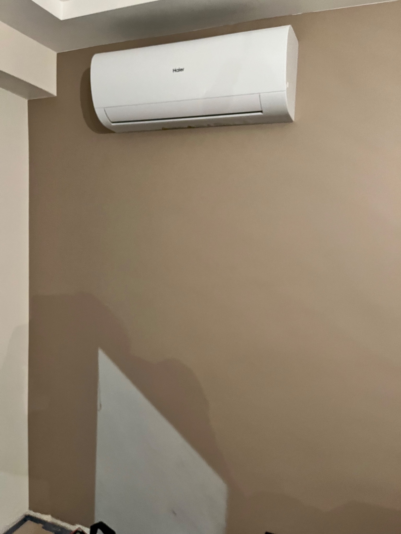 Biały klimatyzator Haier zamontowany na beżowej ścianie w pomieszczeniu z białym sufitem.