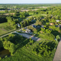 Panoramiczny widok z drona na wiejską okolicę z domami jednorodzinnymi, polami uprawnymi i lasami w letnim świetle.